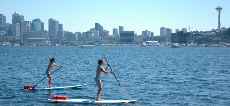 First time out for two women – stand up paddle boarding on a sunny day, Lake Union, Space Needle, South Lake Union view, Gas Works Park, Seattle, Washington, USA