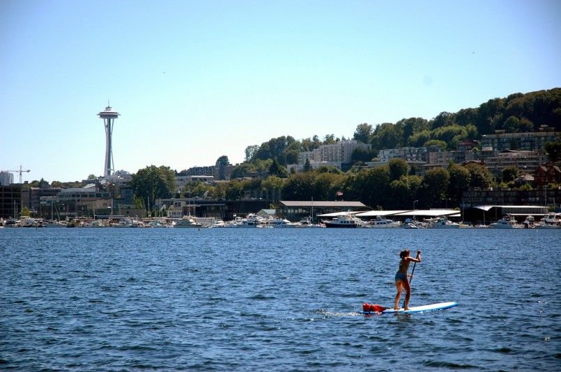 Two of the 3-legged ones, a young woman paddles a surf board across the blue Lake Union, Space Needle in the distance, Seattle, Washington, USA