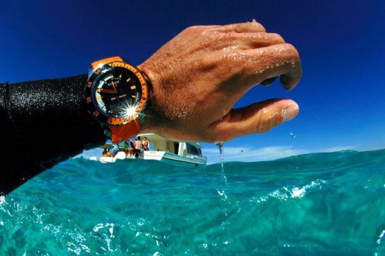 orange and black diving watch on man's wrist in water