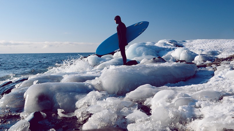 in wetsuit with surfboard on icy shore