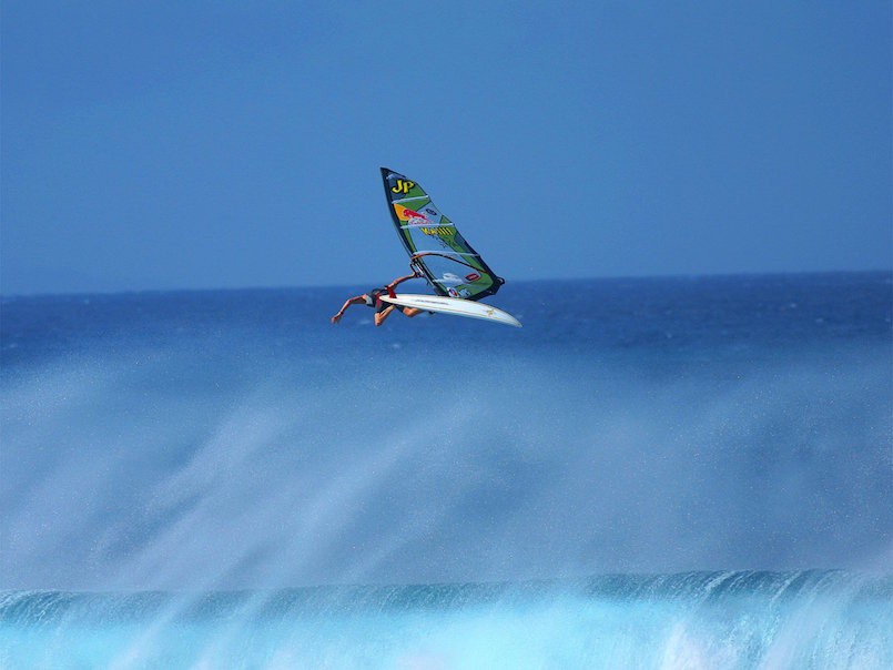 person windsurfing and jumping over a wave