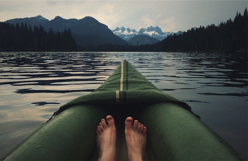 sweat on feet in green kayak on lake with mountains