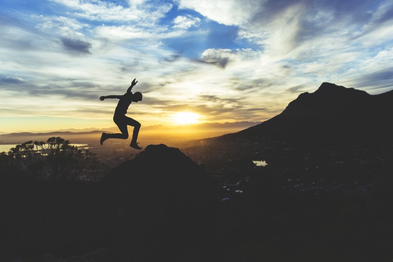man jumping with sunset over city and mountains