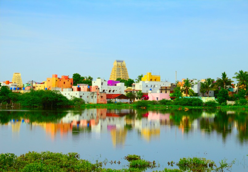 Beautiful scenic view of sacred city Kanchipuram (Kanchi) with colorful traditional houses, gopura of Hindu Temple and bright foliage reflected at calm lake waters, Tamil Nadu, South India