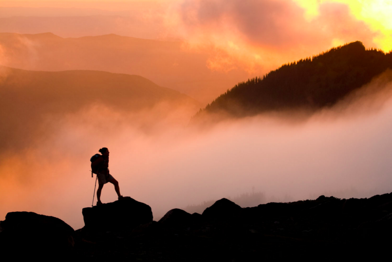 hiker on mountain in clouds at sunset