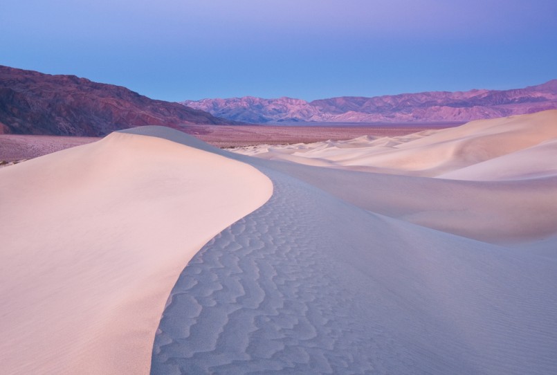 View of a sand dune with mountains in the background from Death Valley National Park. Taken during the early morning light right before sunrise