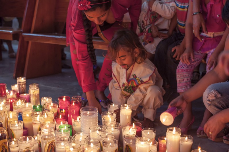 young boy dressed as Juan Diego is helped by his mother as he places a candle on a church floor after a mass celebrating the Feast of Our Lady of Guadalupe