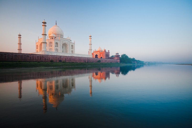 The Taj Mahal glowing red at morning sunrise along the rear riverbank of the holy Jamuna river in Agra, India. Horizontal copy space