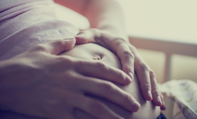 Closeup of pregnant woman holding her hands on her swollen belly shaping a heart, toned retro or instagram effect