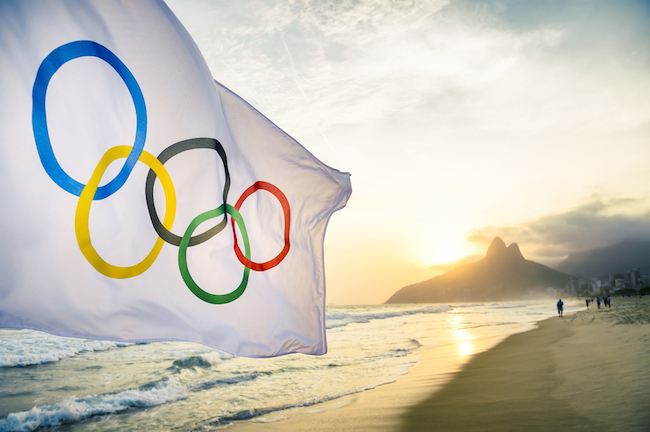 RIO DE JANEIRO, BRAZIL – OCTOBER 27, 2015: An Olympic flag flutters in the wind in front of the sunset skyline at Ipanema Beach.