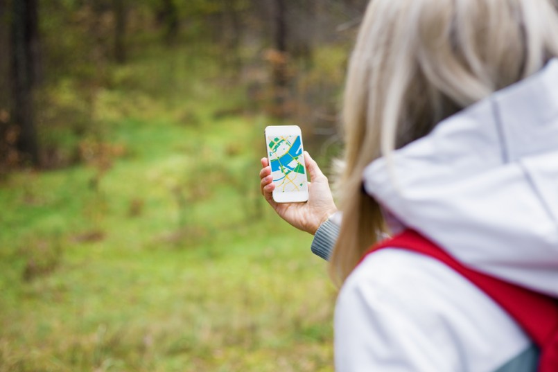 Woman geocaching in forest and using map app on smartphone